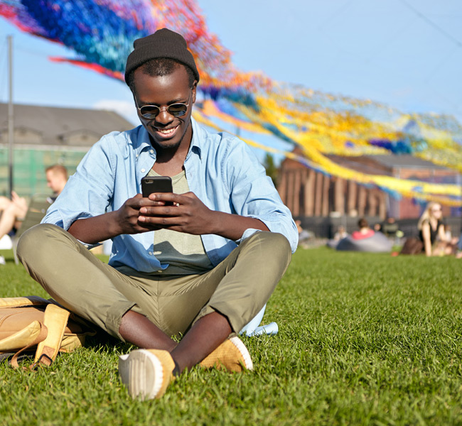 young man sitting at an outside event looking at his phone and smiling